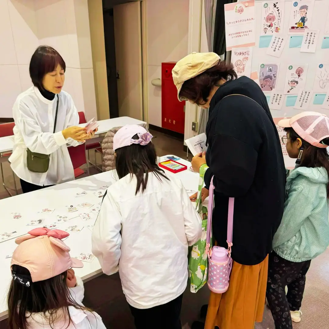 地域のイベントで、カルタを手にしたスタッフと参加者が話す様子
